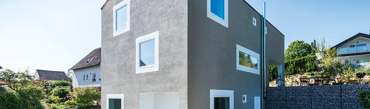 Ein Haus mit einer grauen Fassade und vielen weißen Kunststofffenstern. 