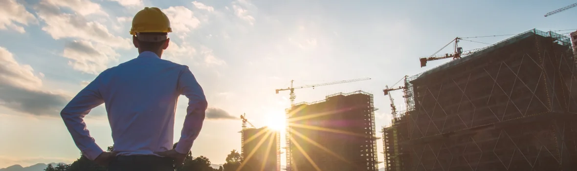 Architekt steht vor einer Großstadt im Bau mit Kränen und dem Sonnenuntergang im Hintergrund