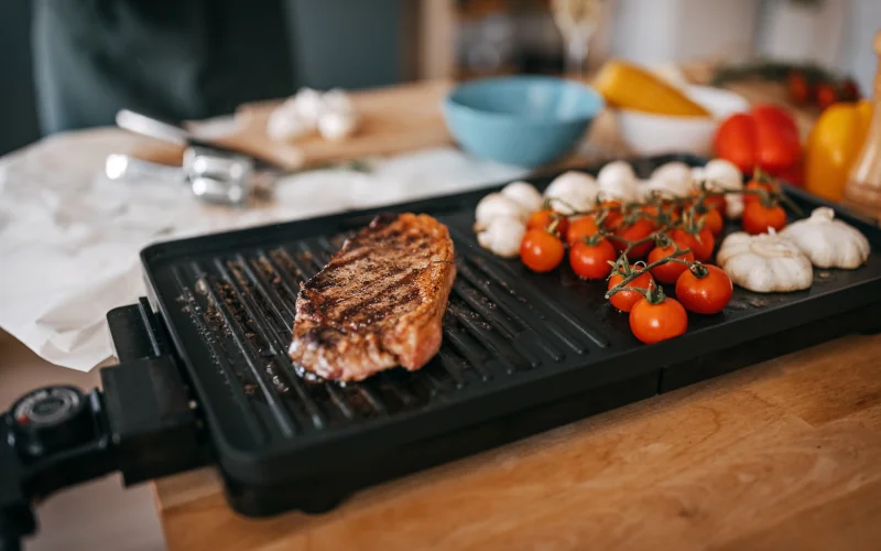 Elektrogrill auf dem Esstisch mit Gemüse und Fleisch darauf