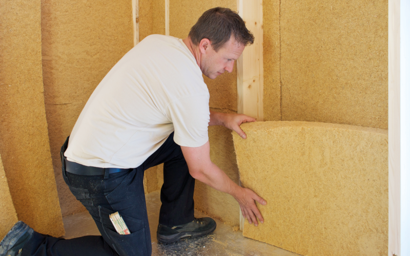 Ein Mann setzt eine Dämmplatte zwischen Holzständer einer Wandkonstruktion ein.