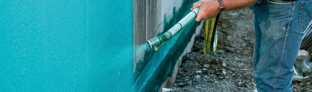 Der blaue Abdichtungsschlamm wird durch einen Schlauch auf eine Hauswand aufgetragen.