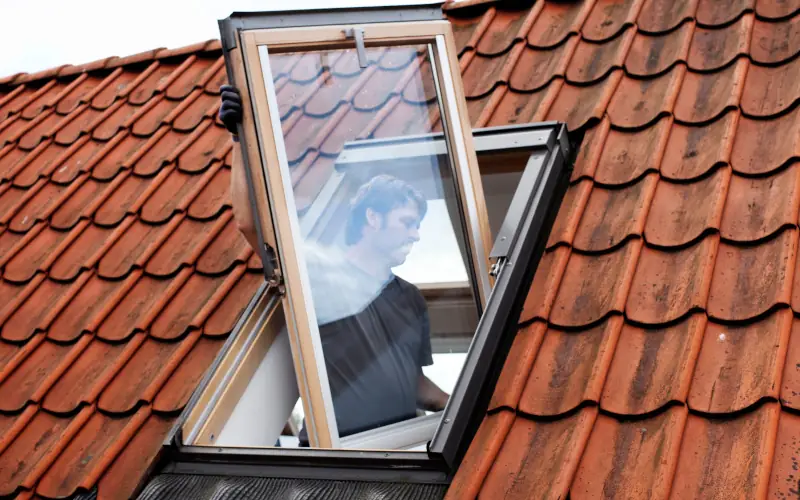 Mann schaut durch Dachfenster auf Ziegeldach.