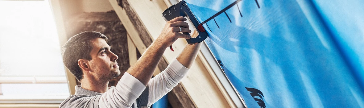 Mann tackert Plastikplane an Wand. 