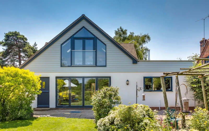 Einfamilienhaus mit Garten und vielen Fenstern. Fassadendielen sind im oberen Bereich verbaut. 