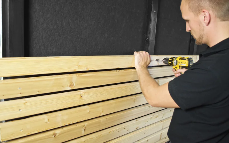 Mann schraubt Holzlatten an Fassade 
