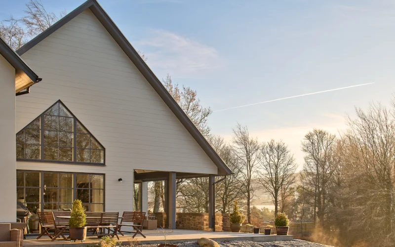 Wohnhaus mit Terrasse im Waldgebiet mit weißen Fassadenplatten angestrahlt von der Sonne