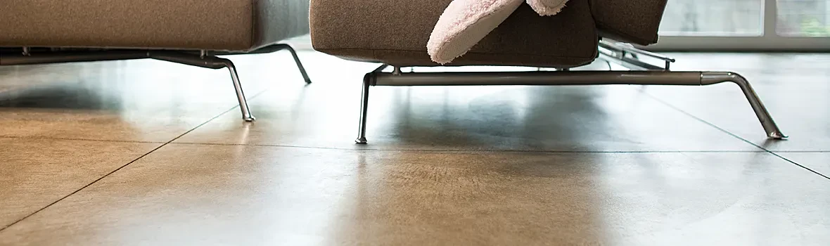 Das Bild zeigt einen modernen Innenraum mit großformatigem Bodenbelag und den schlanken Metallfüßen eines Sofas im Vordergrund.