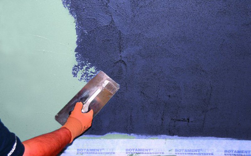 Handwerker spachtelt blaue Masse an die Wand