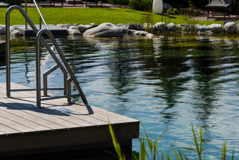 Schwimmteich mit Steinen und Leiter von einem Holzsteg aus