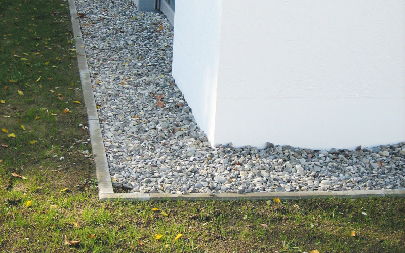 Ein Kiesbett ist neben einer weißen Hauswand angelegt