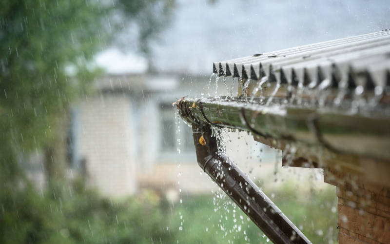 Wasser läuft an einem Dachherunter in eine Regenrinne 