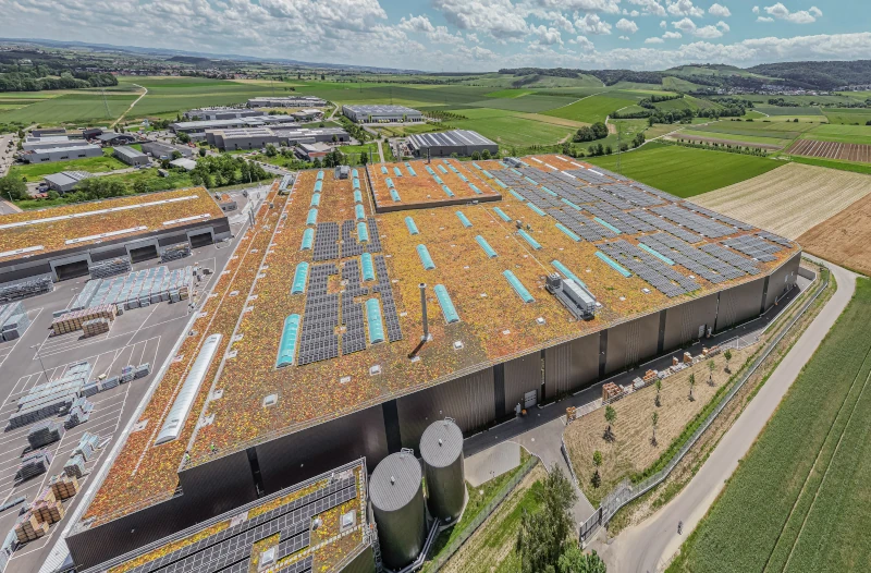 Ein Flachdach ist bepflanzt und mit Photovoltaikanlagen und kleinen Dachfenstern, sie sich öffnen lassen, ausgestattet. 