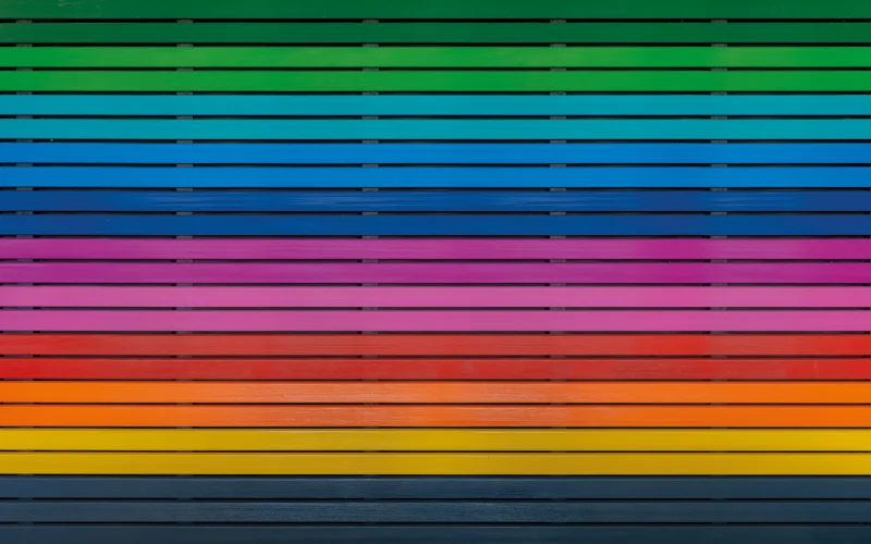 verschiedene Holzlatten an der Fassade in bunten Farben, angeordnet wie ein Regenbogen 