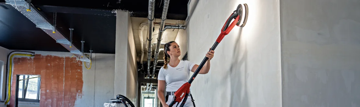Frau saugt eine Wand mit einem Sicherheitsstaubsauger von FLEX ab