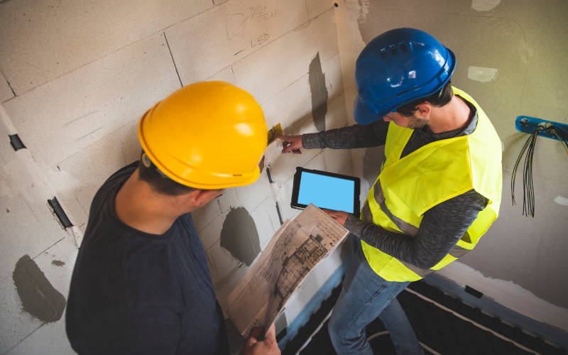 Zwei Handwerker mit iPad in der Hand stehen auf Baustelle