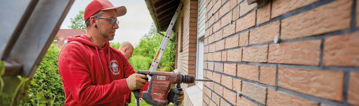 Handwerker bearbeitet Hauswand mit Werkzeug.