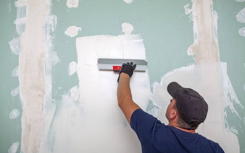 Mann verstreicht Spachtel an einer Wand im Innenraum