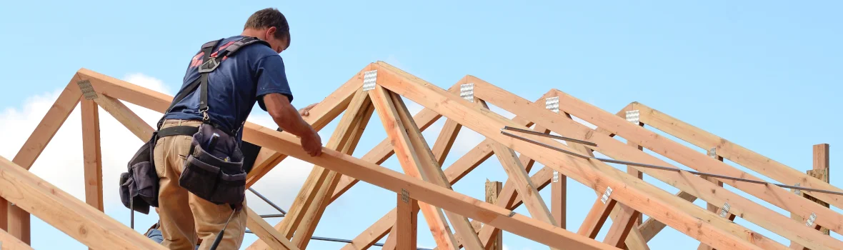 Handwerker sitzt auf einer Dachstuhl-Holzkonstruktion eines Daches im Bau