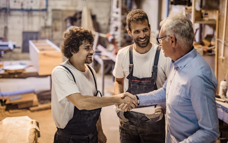 Zwei Handwerker schütteln Mann die Hand in der Werkstatt