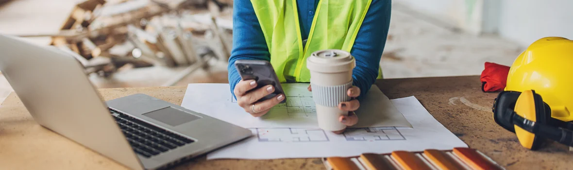 Bauarbeiterin auf der Baustelle mit einem Laptop vor sich stehend