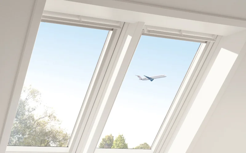 Dachfenster mit Blick von innen nach außen, draußen fliegt ein Flugzeug