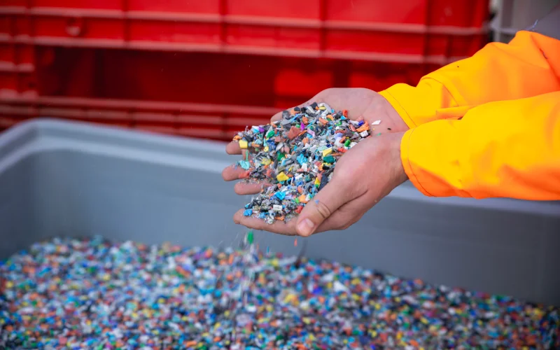 Mit den Händen werden aus einer großen Kiste kleine, bunte Kunststoffteilchen geholt
