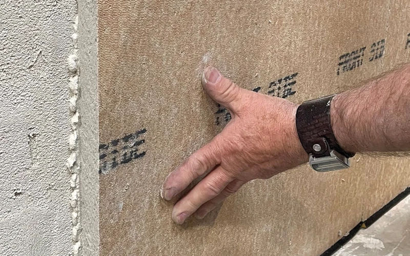 Eine Hand drückt eine Bauplatte an eine Wand.