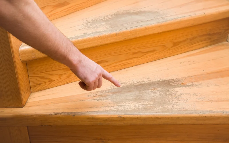 Mann zeigt auf Abnutzungen an Holzstufen einer Treppe 