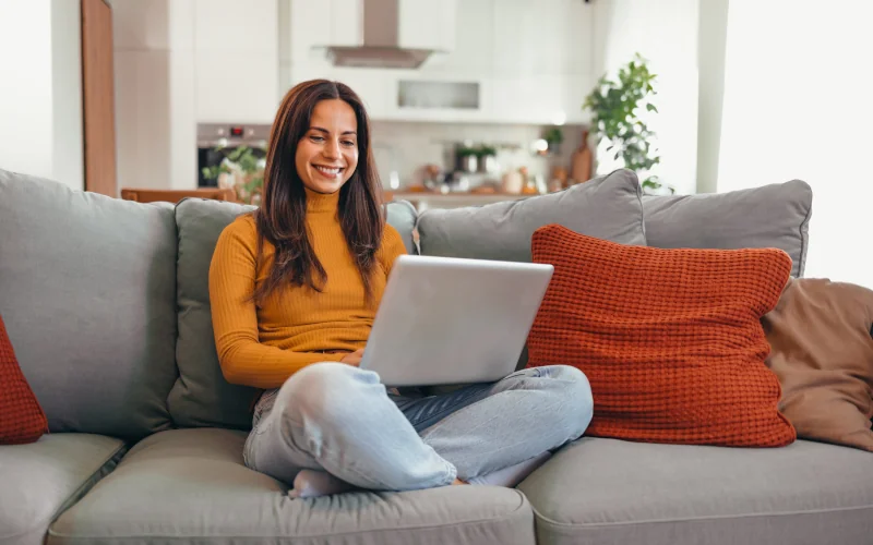 Frau sitzt auf einem Sofa mit einem Laptop auf dem Schoß