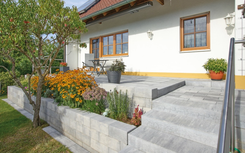 Gartenmauer der Marke KANN mit Terrassenmöbeln und Blumenbeeten.