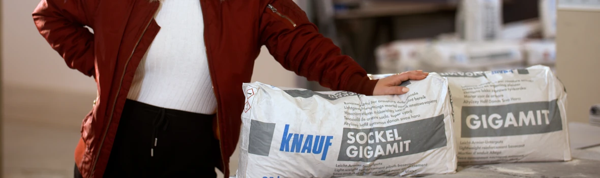 Frau steht neben Säcken mit Knauf Sockel Gigamit 
