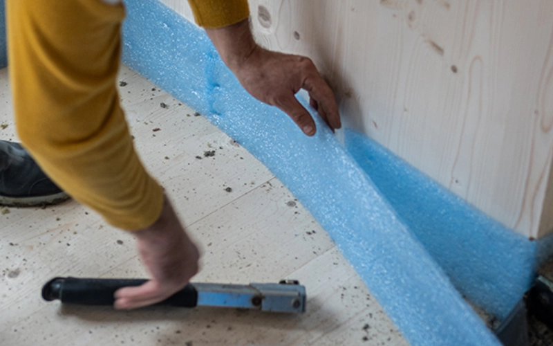 Ein Handwerker verlegt Dämmmaterial als Schallschutz in einem Wohngebäude.