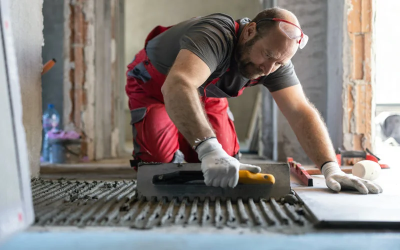 Handwerker bereitet Klebeuntergrund zum Fliesenverlegen vor 