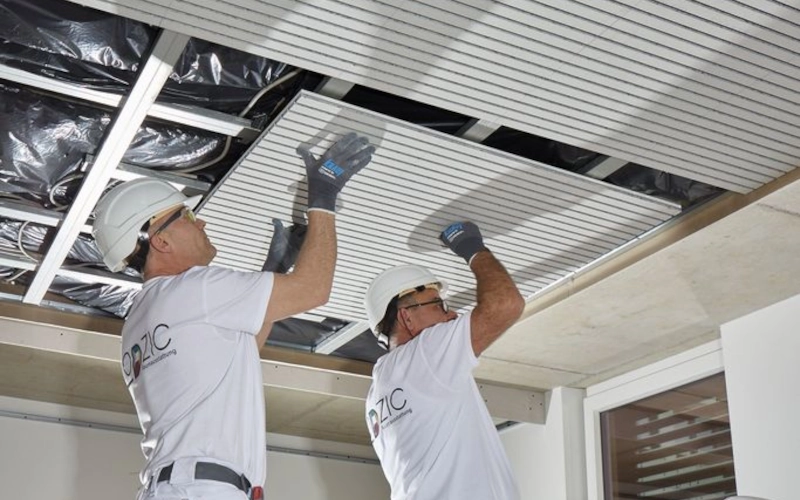 Zwei Handwerker bringen die Akustiklösung Cleaneo Stripe von Knauf an der Decke an