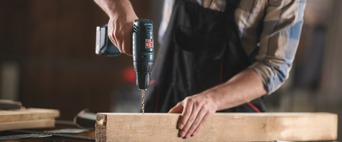 Mit einem Bohrer bohrt ein Mann in eine Holzlatte