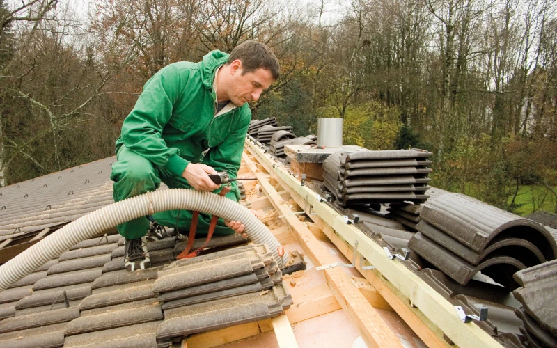 Handwerker befüllt ein Dach von oben mit Dämmmaterial.