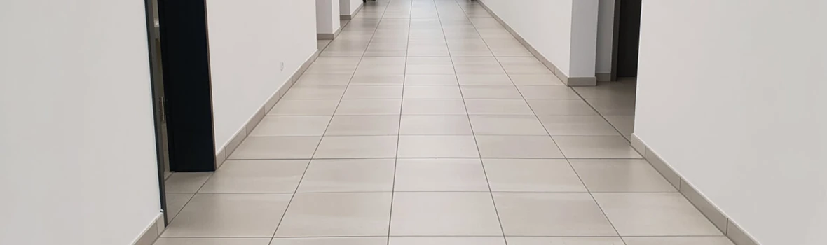 Flur in einem Gebäude mit weißen Wänden, Fliesen und schwarzen Fugen 