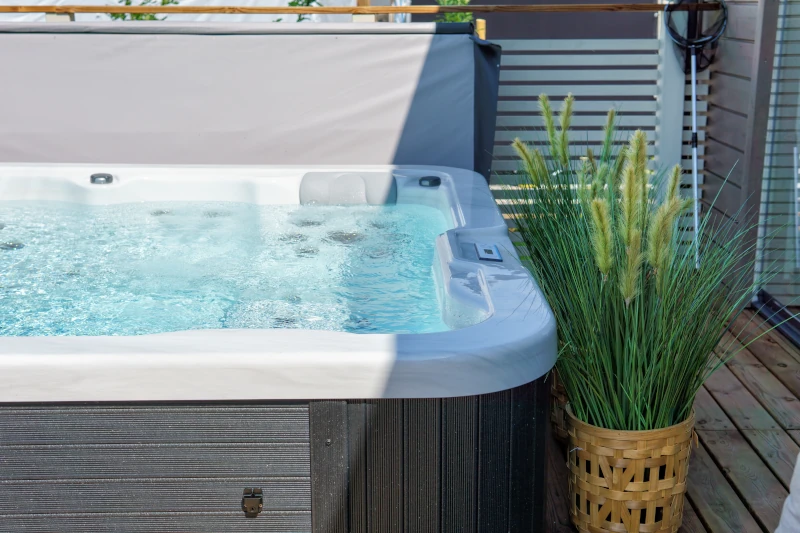 Whirlpool auf Holzterrasse, sprudelndes Wasser, dekorative Pflanze im Korb, entspannende und moderne Atmosphäre.