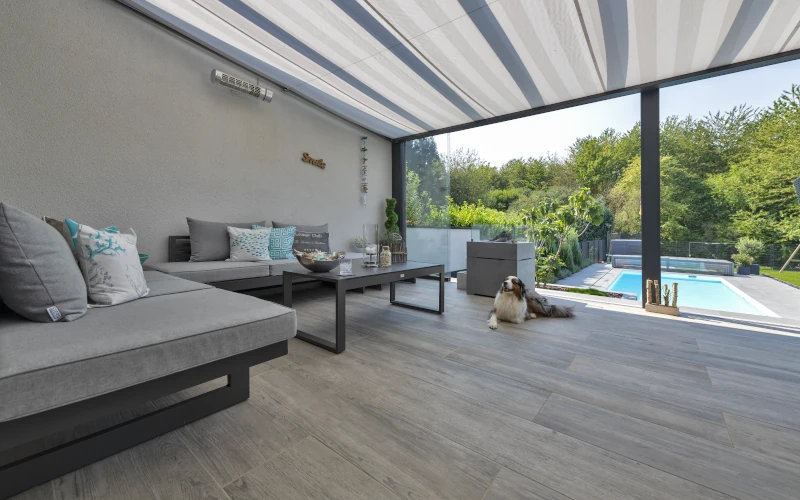 Terrasse mit einer weitreichenden Pergola und Pool im Hintergrund 