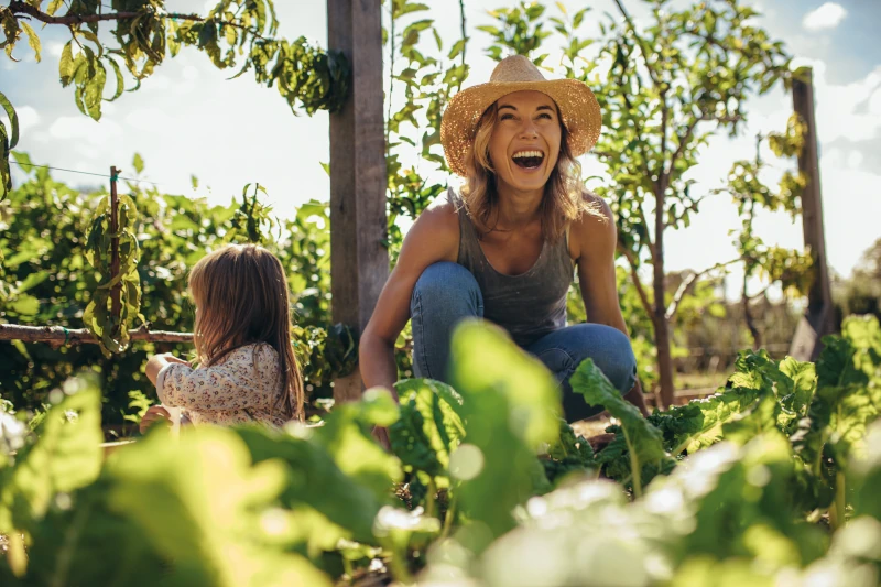 glückliche Frau mit Kind im Garten zwischen vielen Grünpflanzen