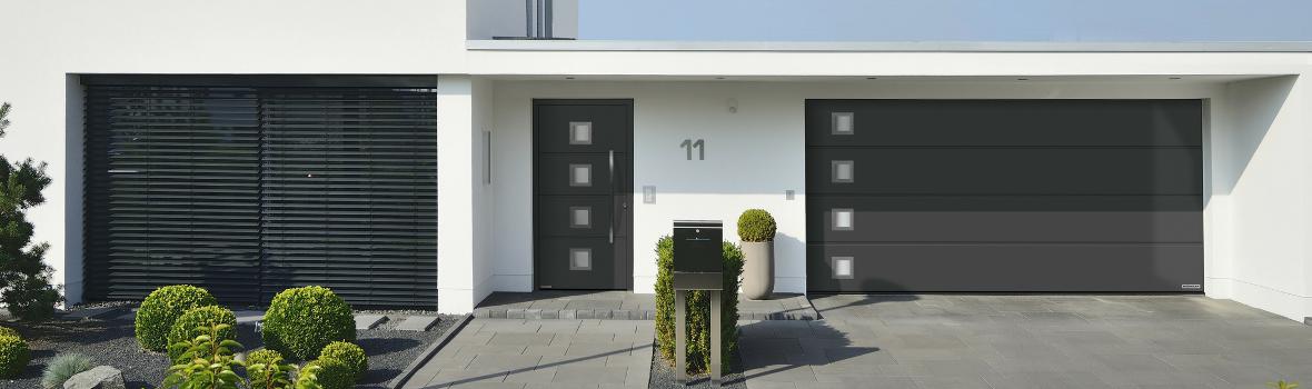 Graue Haustür und Garagentor mit Auffahrt