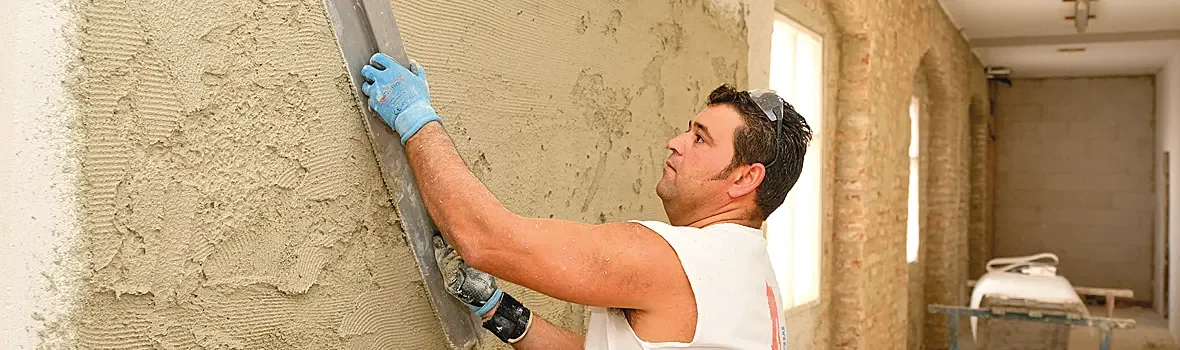 Handwerker verstreicht braune Masse mit einem Richtscheit an der Wand