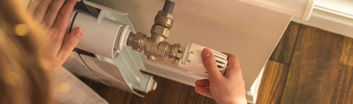 Frau dreht am Thermostat einer Heizung