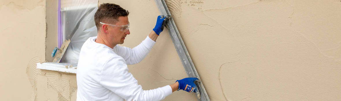 Handwerker verstreicht braune Masse an Fasse mit langem Richtscheit
