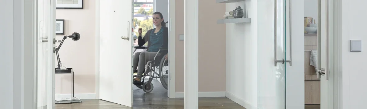 Frau im Rollstuhl öffnet eine barrierefreie Tür mit einer smarten Steuerung
