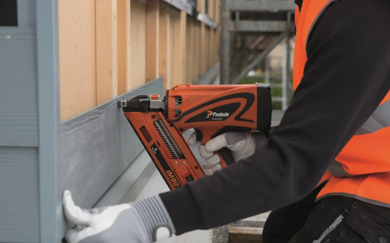 Arbeiter bringt Fassadendielen an Holzrahmen an der Fassade an mit Pressluft-Nadelpistole