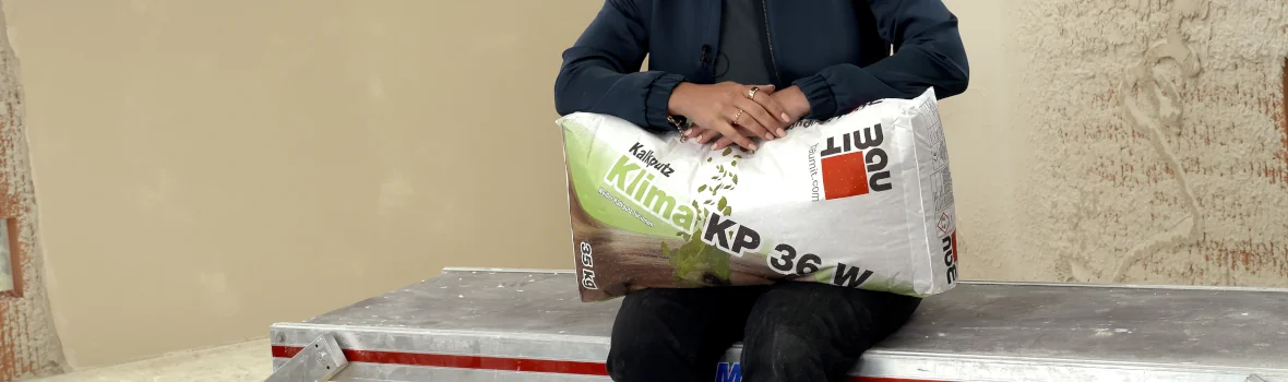 Frau sitzt auf Metallunterlage mit einem Sack Kalkputz in der Hand 