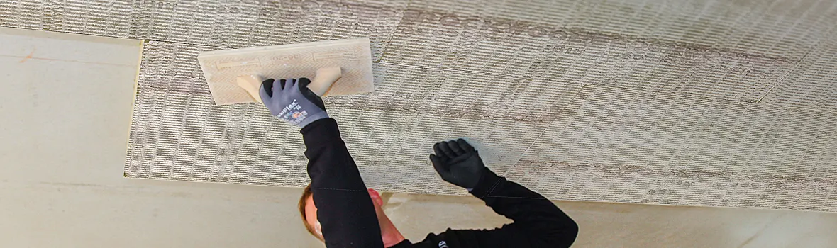 Handwerker drückt Dämmmaterial an die vorher mit Kleber vorbereiteten Stellen der Kellerdecke