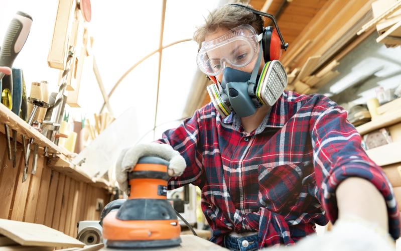 Tischlerin schleift Holz mit einer Schleifmaschine in einer Werkstatt