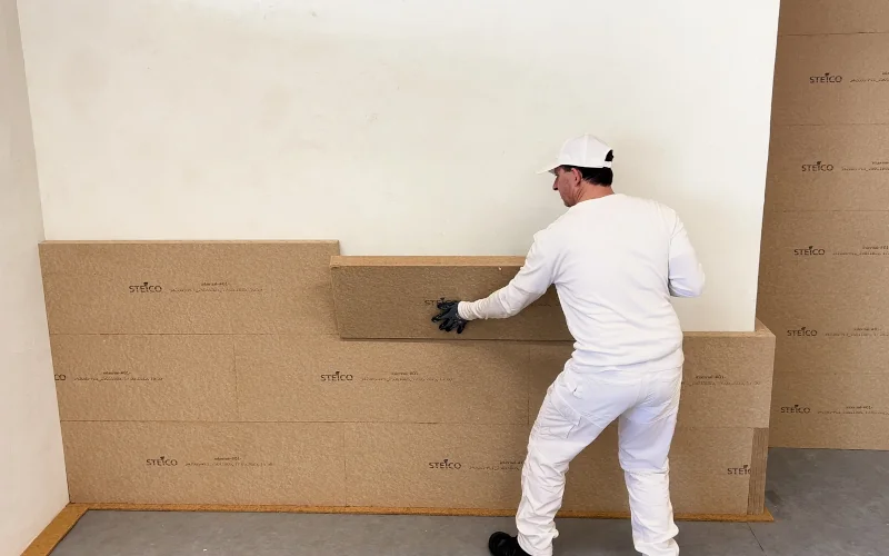 Handwerker bringt Dämmplatten an einer weißen Wand an